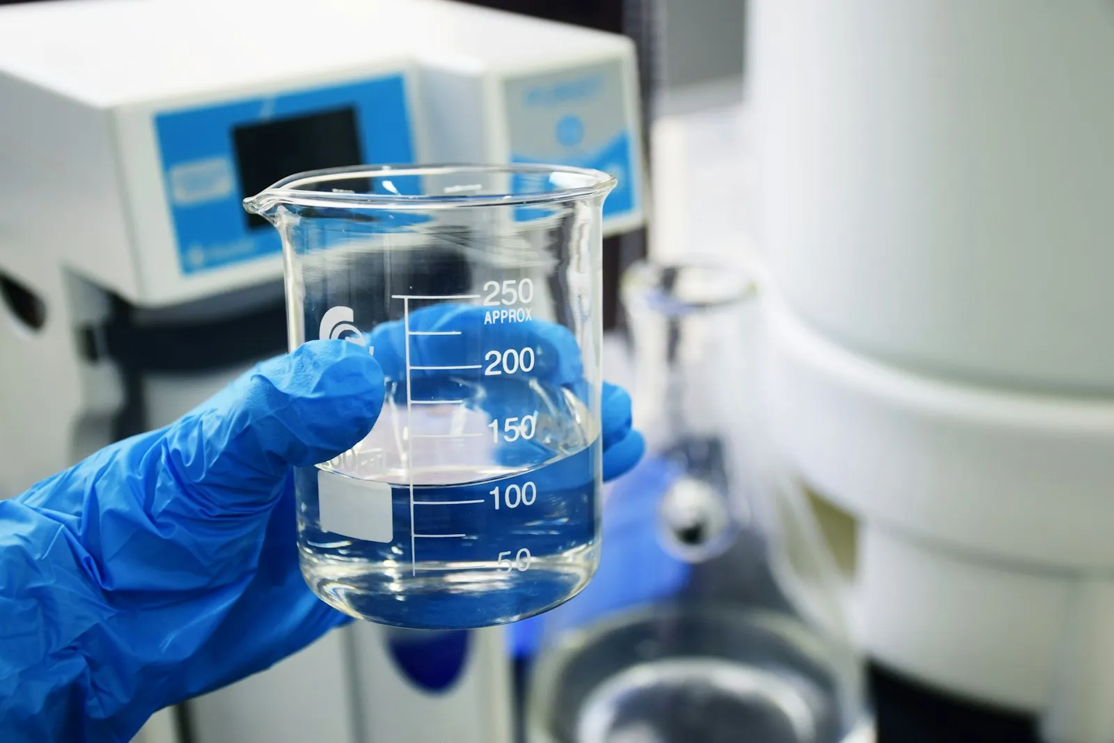 Zlewka z cieczą w dłoni w rękawiczce laboratoryjnej